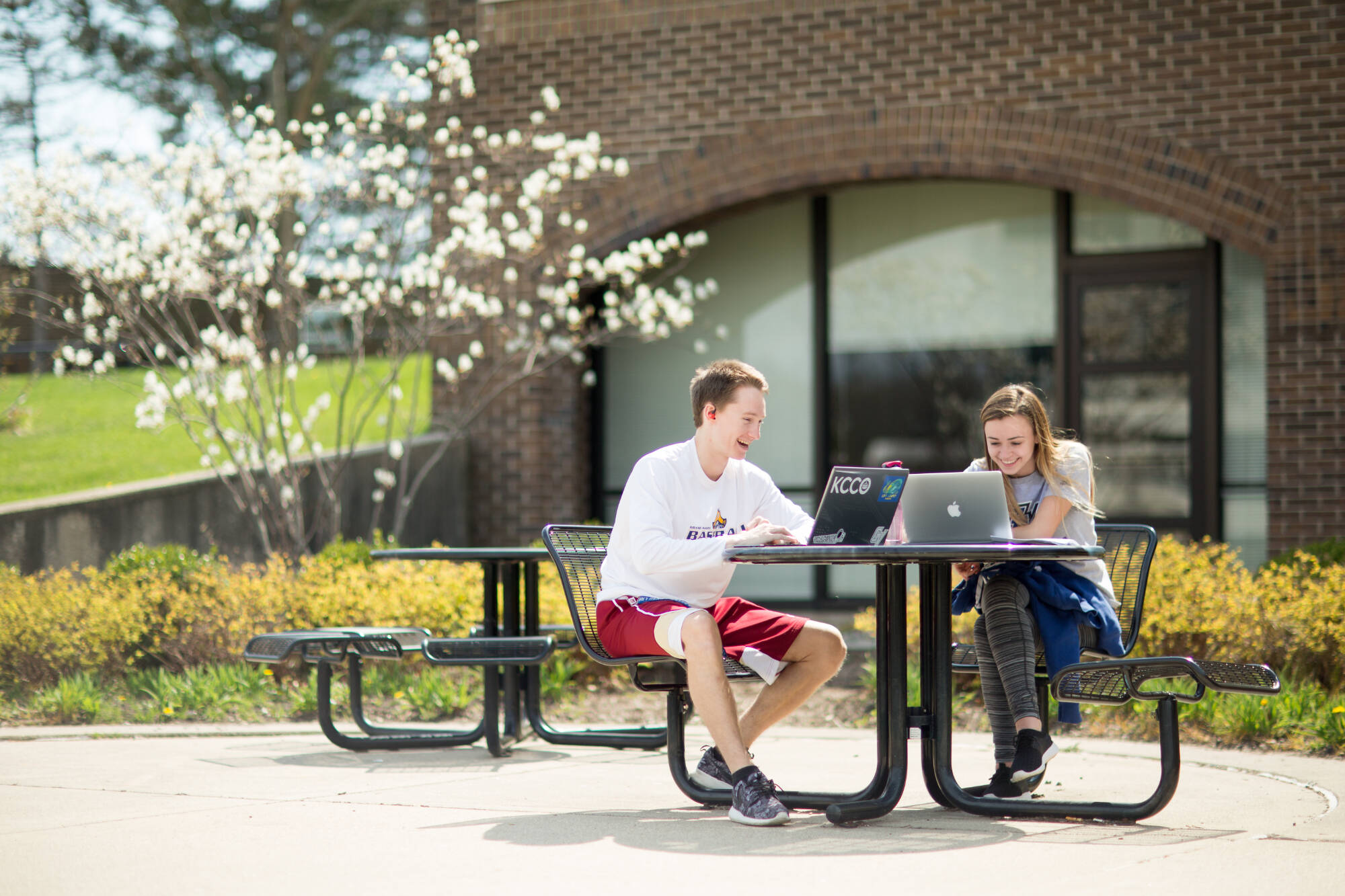 Two students working on their laptops near the Kirkhof Center in a sunny day